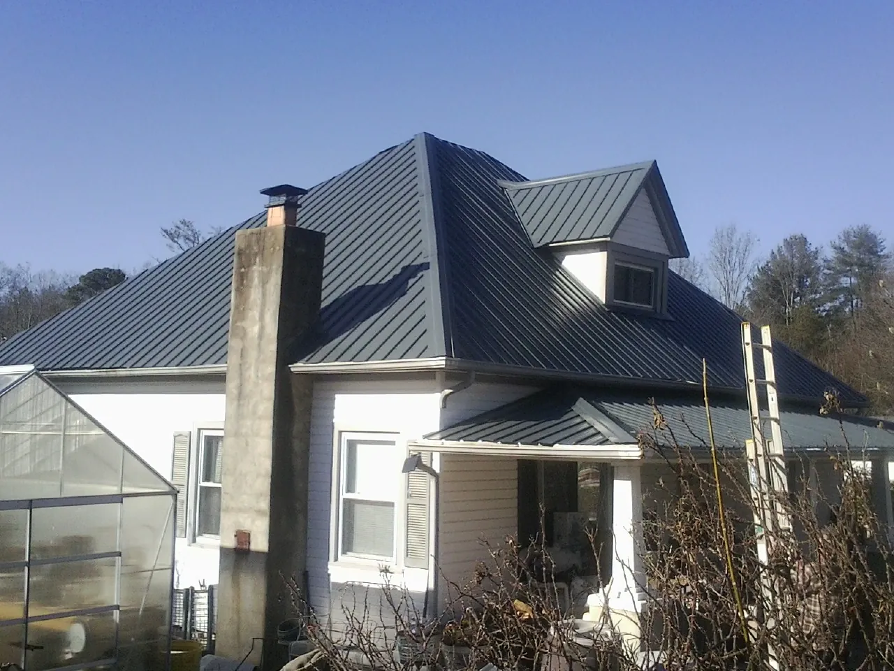 Dark blue standing seam metal roof on a white farmhouse with dormer — Slate & Tile Roof Repair by Roofing Brothers in Pilot Mound
