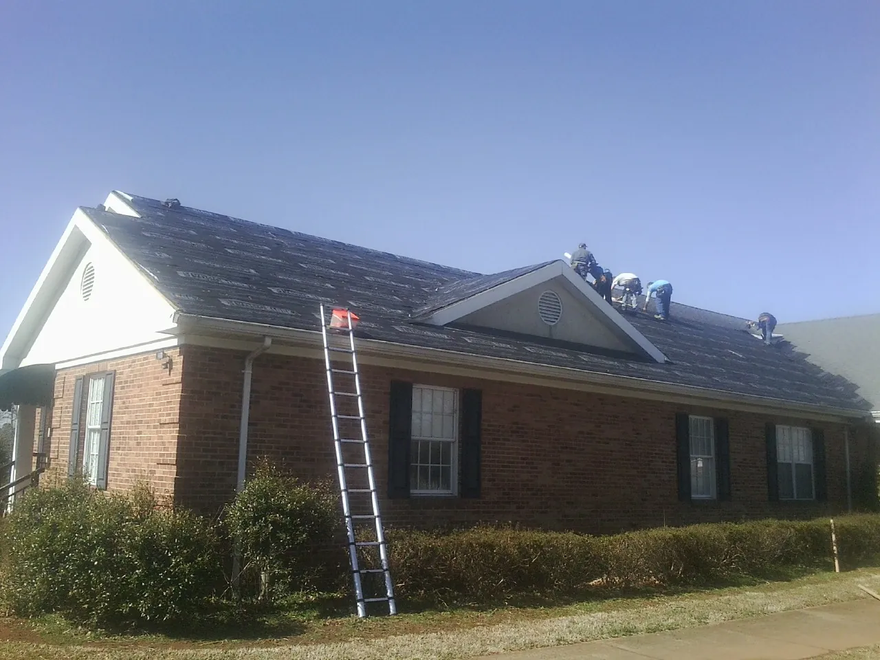 Crew tearing shingles off a brick ranch roof with a ladder set — Metal Roof Repair work by our crew in Pilot Mound