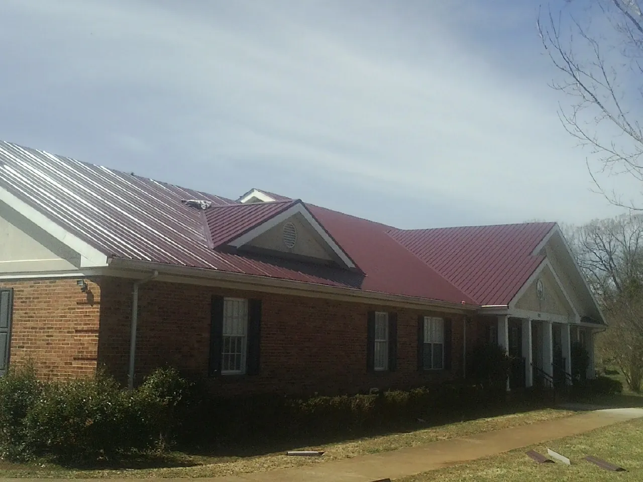 Red metal roof with gabled entries on a long brick building, from a Hail Damage Roof Repair job in Pilot Mound