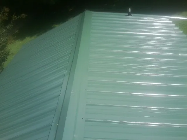 New green metal panels meeting at the ridge of a roof — Flat Roof Repair work by our crew in Pilot Mound