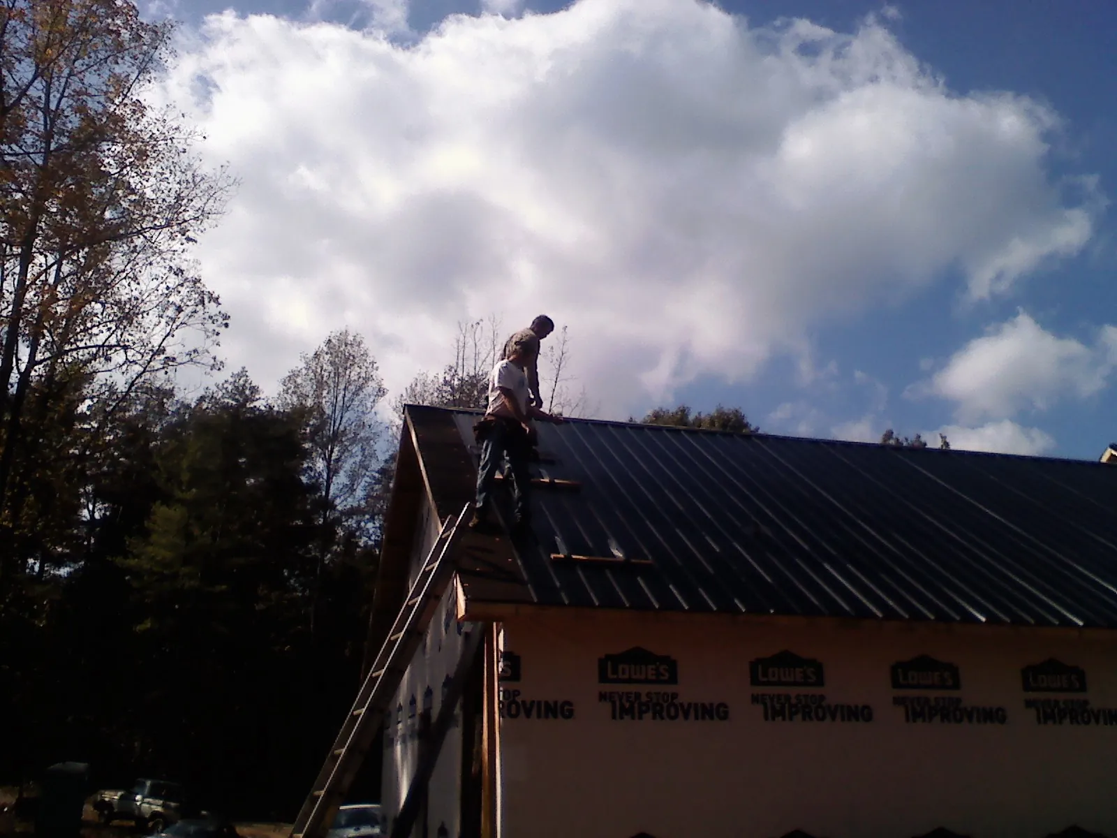 Roofer fastening dark metal panels high against a cloudy sky, from a Roof Inspection job in Pilot Mound