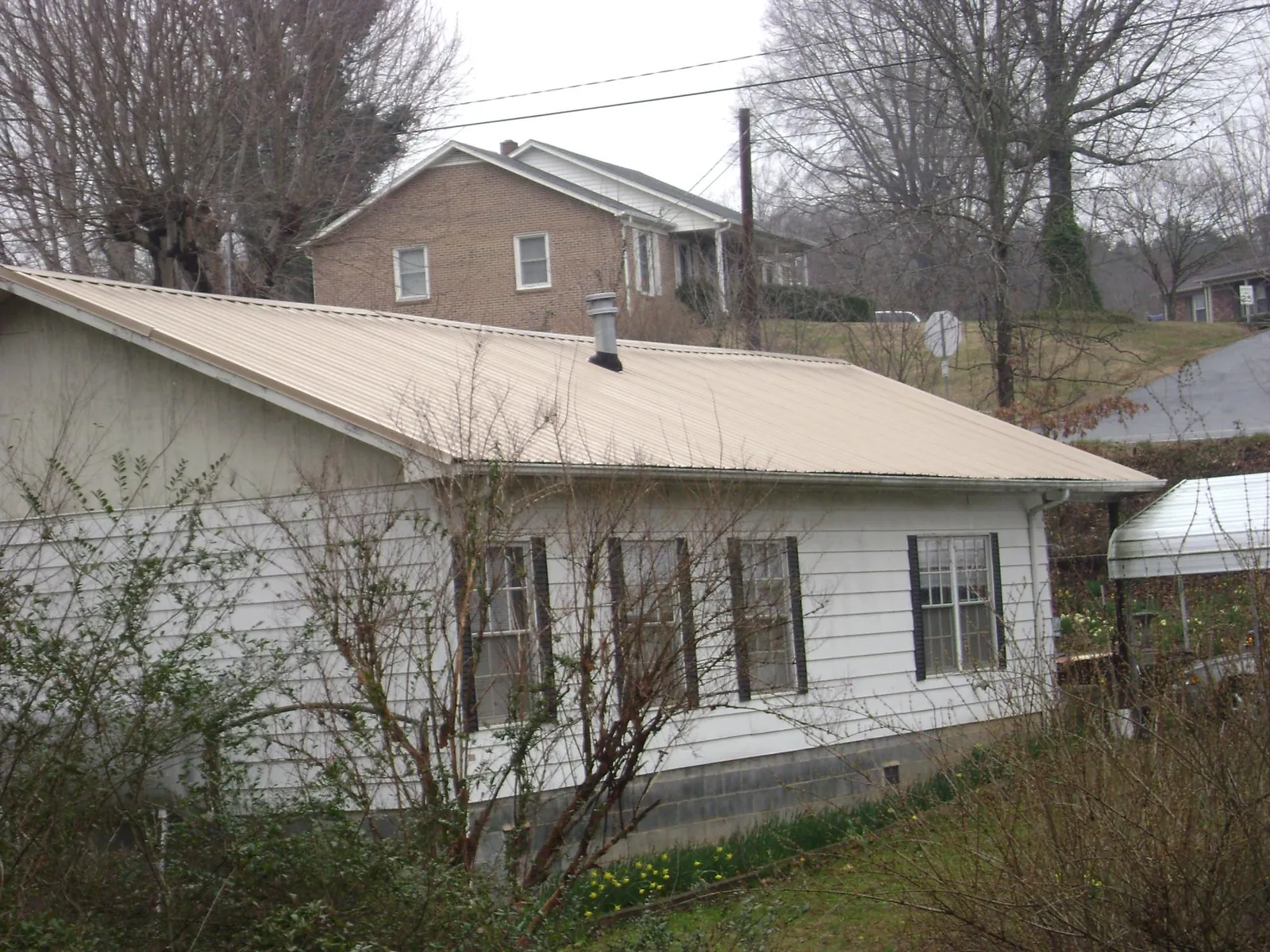 Tan metal roof on a white sided house set into a hillside — Commercial Roofing by Roofing Brothers in Pilot Mound