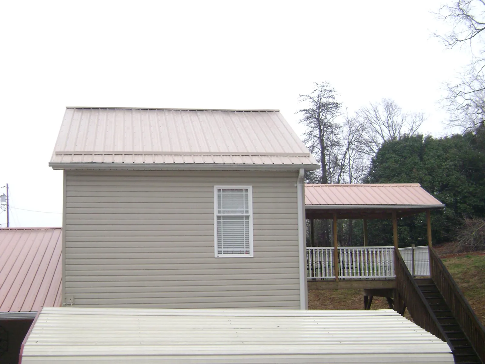 Tan metal roofs on a two story addition and attached porch, from a Roof Replacement job in Pilot Mound